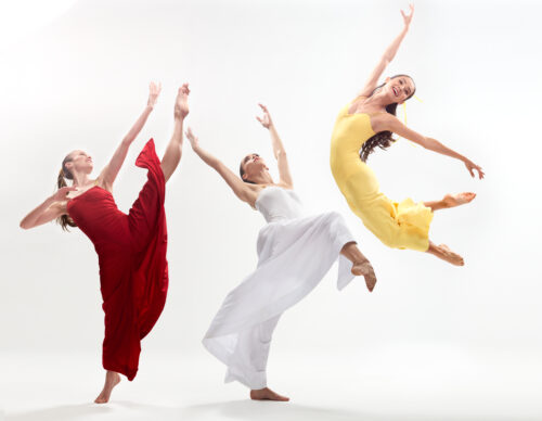 dancers in bright red, white, and yellow fabric jumping and moving with a white background